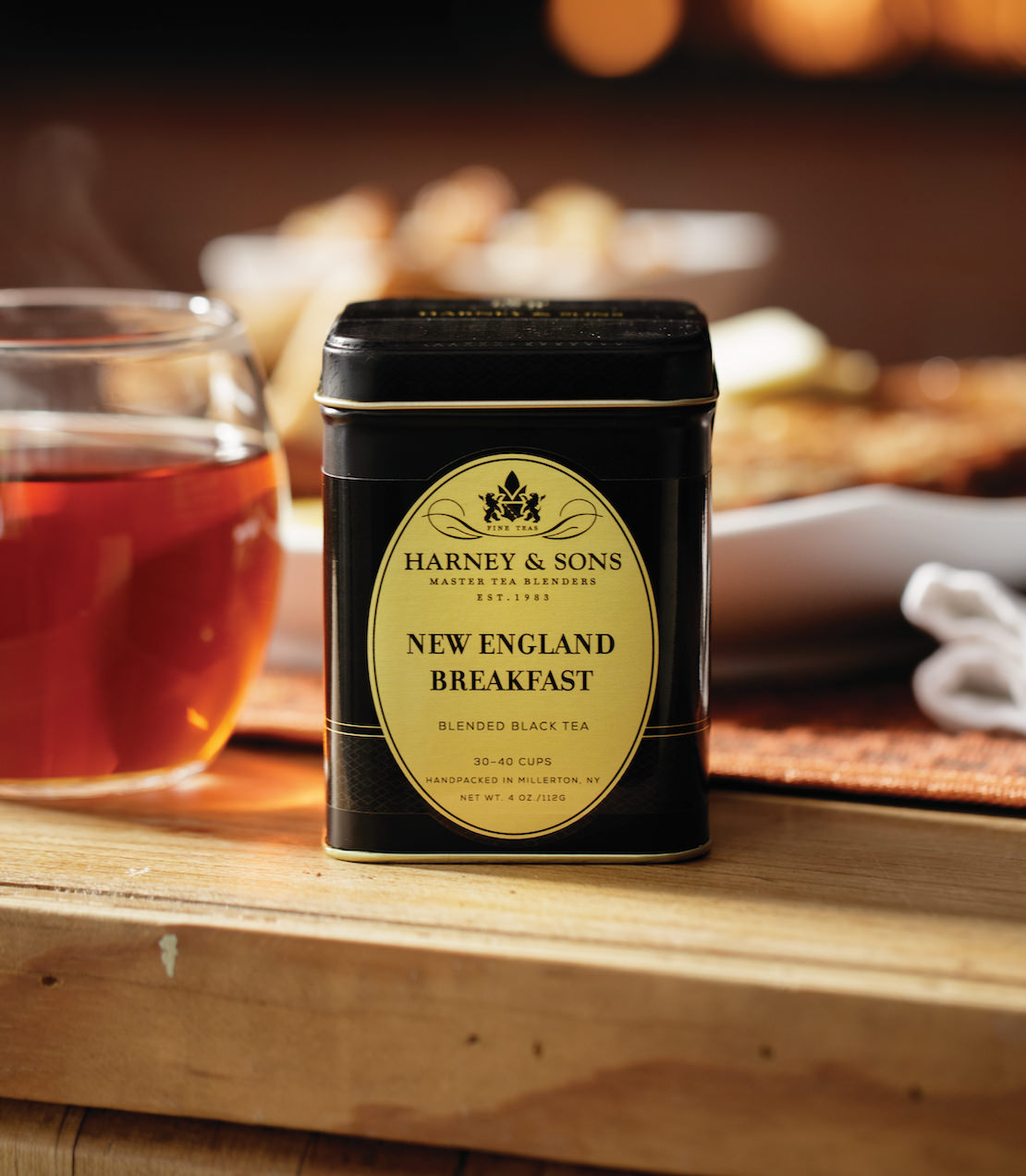 Harney & Sons New England Breakfast black tea tin on a wooden table, with a cup of tea in the background.