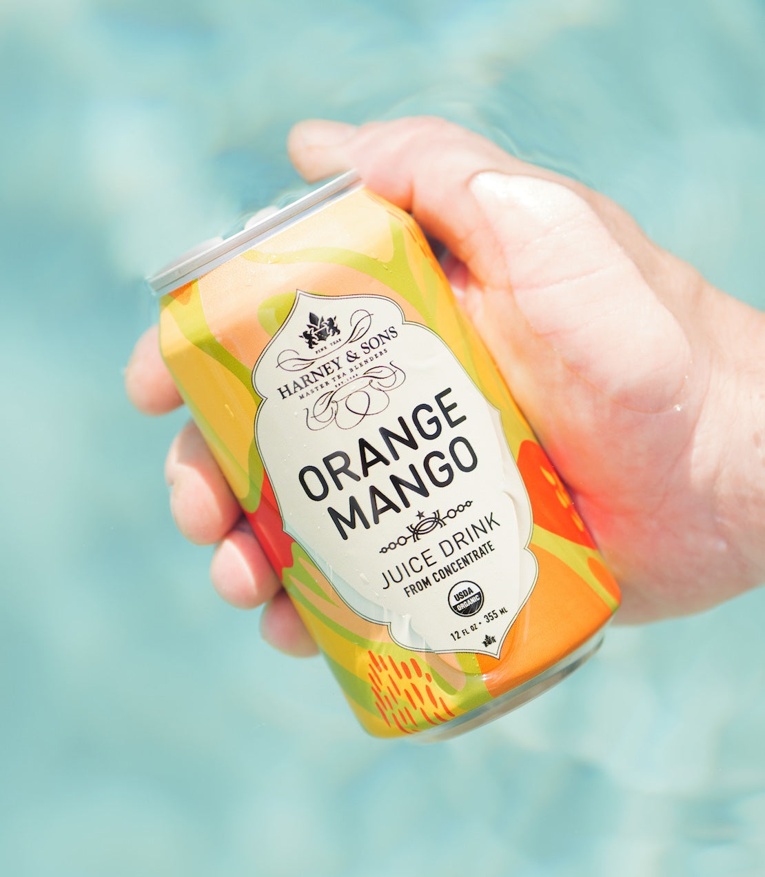 Hand holding a can of Orange Mango juice drink with a blurred blue background.