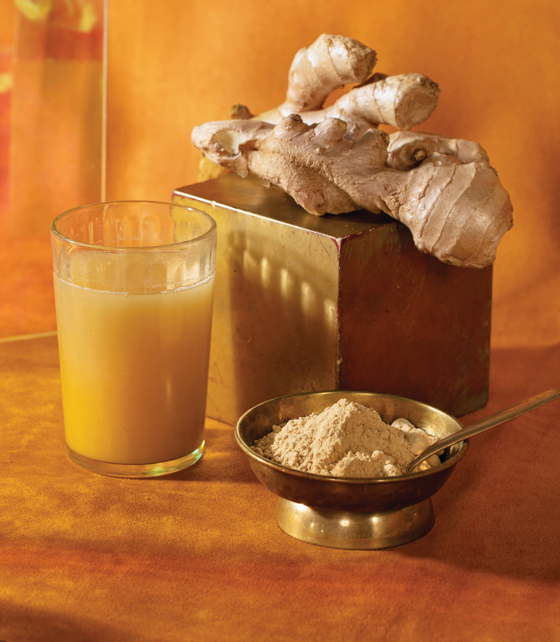 Organic ginger powder in a bowl with a glass of ginger drink and fresh ginger root on a golden background.