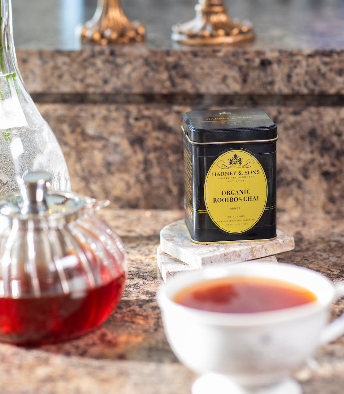 Organic Rooibos Chai tea tin with a cup of tea and teapot on a marble surface.