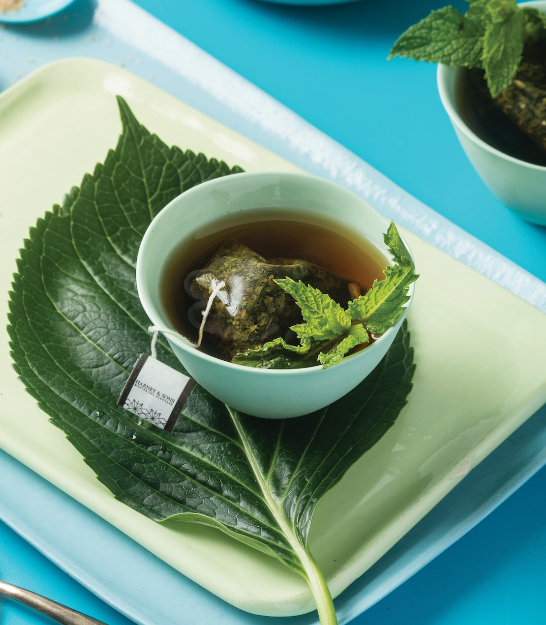 Peppermint herbal tea sachet steeping in a light green cup on a leaf, showcasing a refreshing beverage setup.