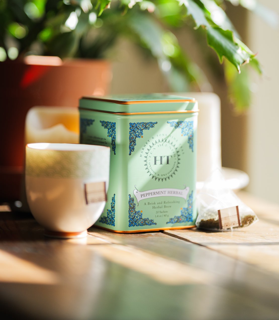 Green tin of Peppermint Herbal tea sachets, featuring decorative design, next to a teacup and sachet.