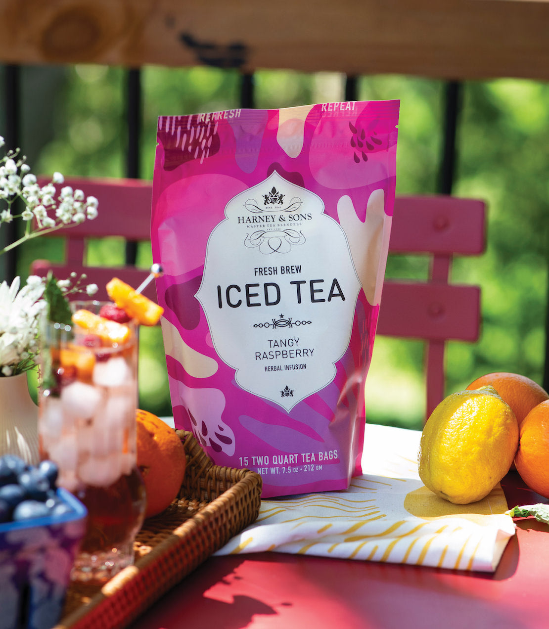 Brightly colored packaging of Harney & Sons Raspberry Herbal Fresh Brew Iced Tea, surrounded by fruits and a refreshing drink.