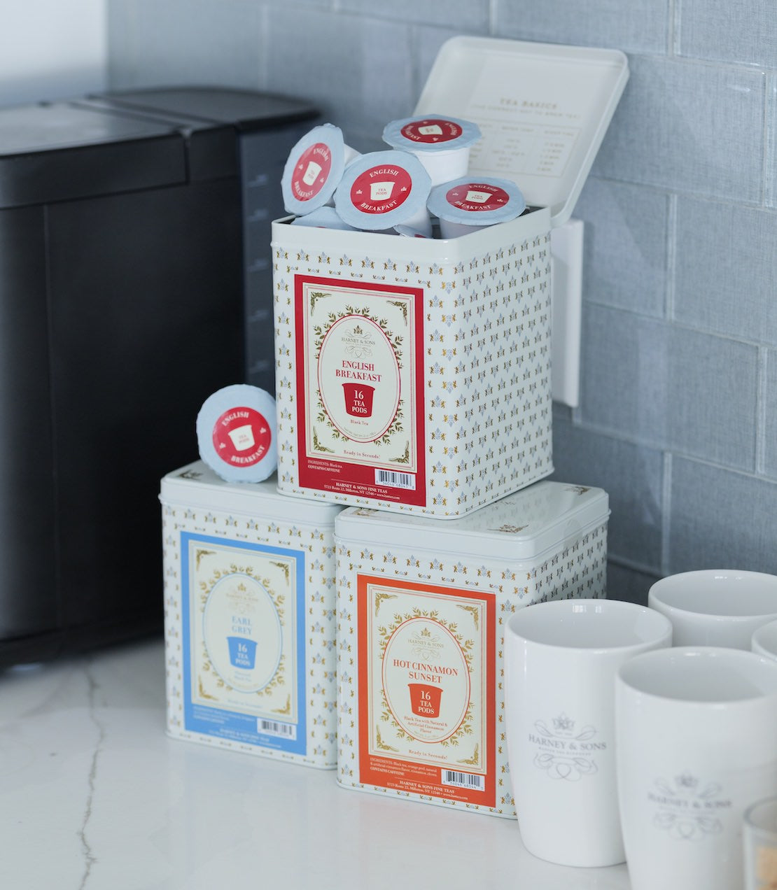 Stack of tea pods canisters on a kitchen counter. English Breakfast, Earl Grey, and Hot Cinnamon Sunset are pictured.