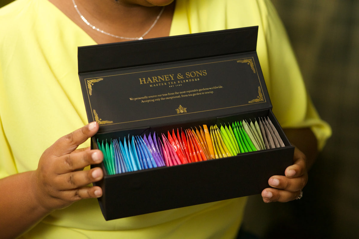 Harney & Sons Teabag & Honey Sampler held open, showing rows of colorful wrapped teabags in the black and gold gift box