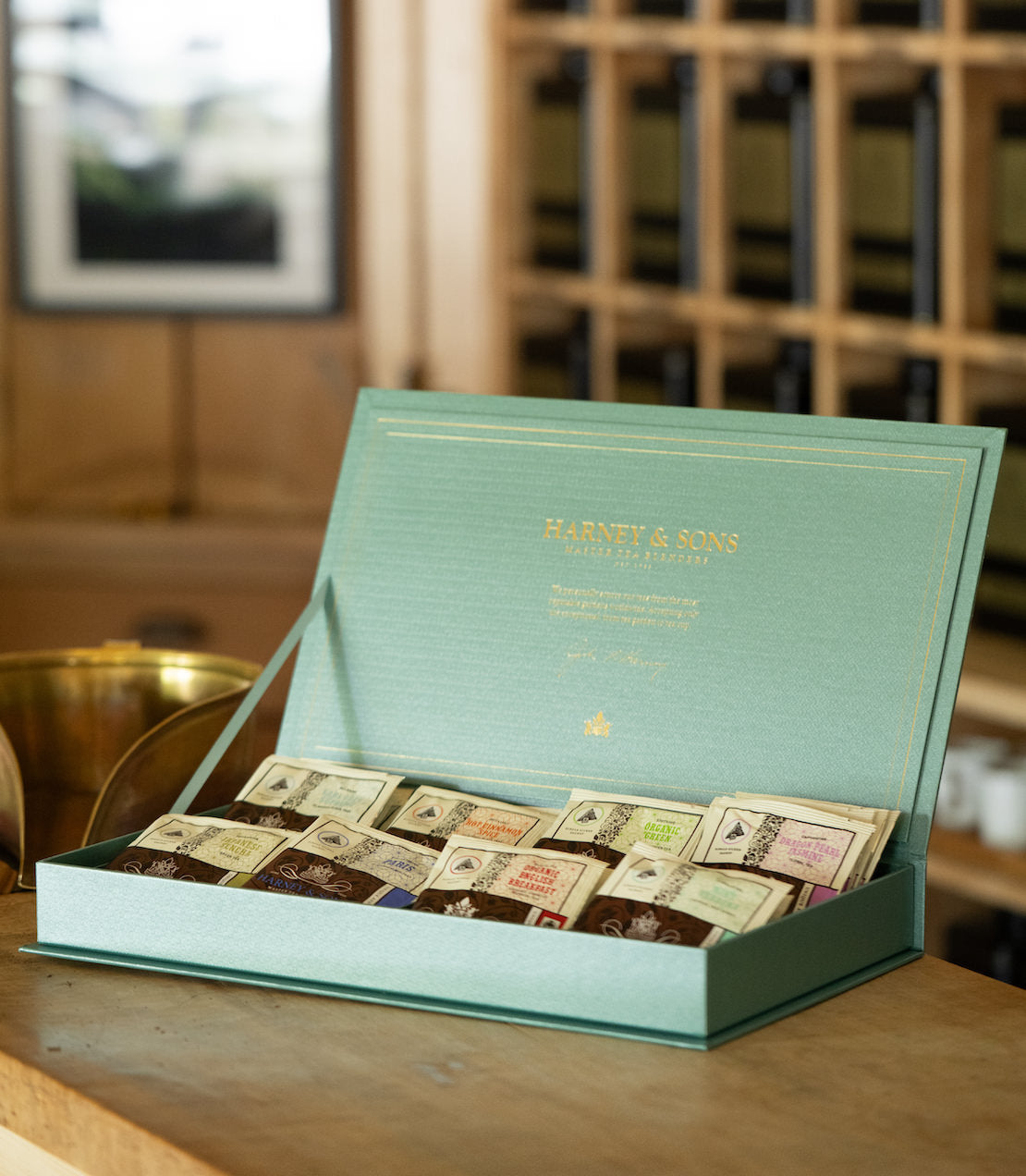 Open teal tea chest with eight teas on a wooden surface, blurred background.