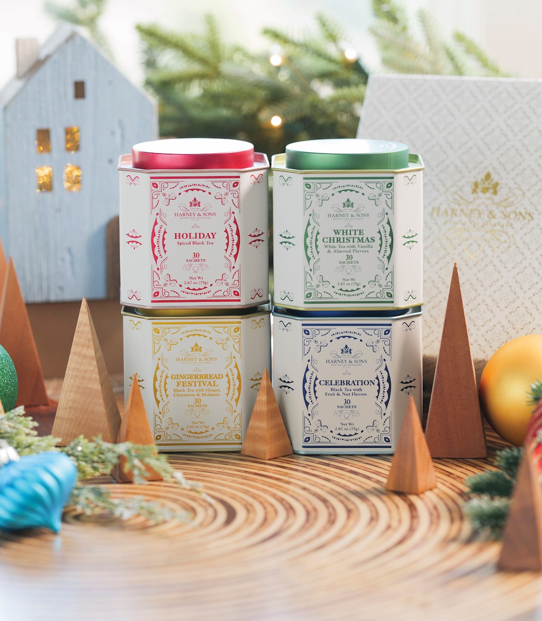 Four decorative tea sachet tins labeled Holiday, White Christmas, Gingerbread Festival, and Celebration, arranged on a festive table.