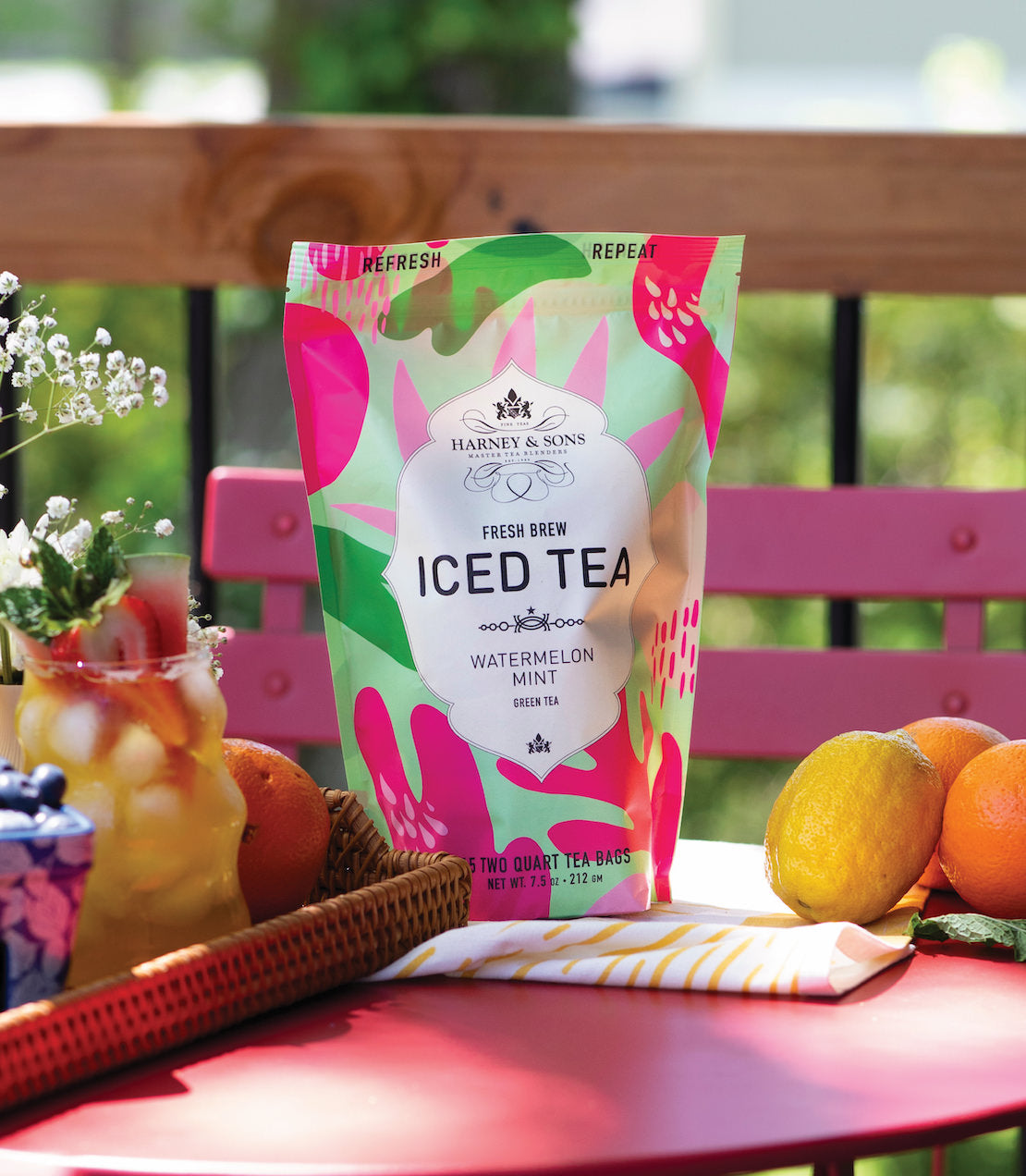 Colorful packaging of Harney & Sons Watermelon Mint Fresh Brew Iced Tea on a table with fruits and flowers.