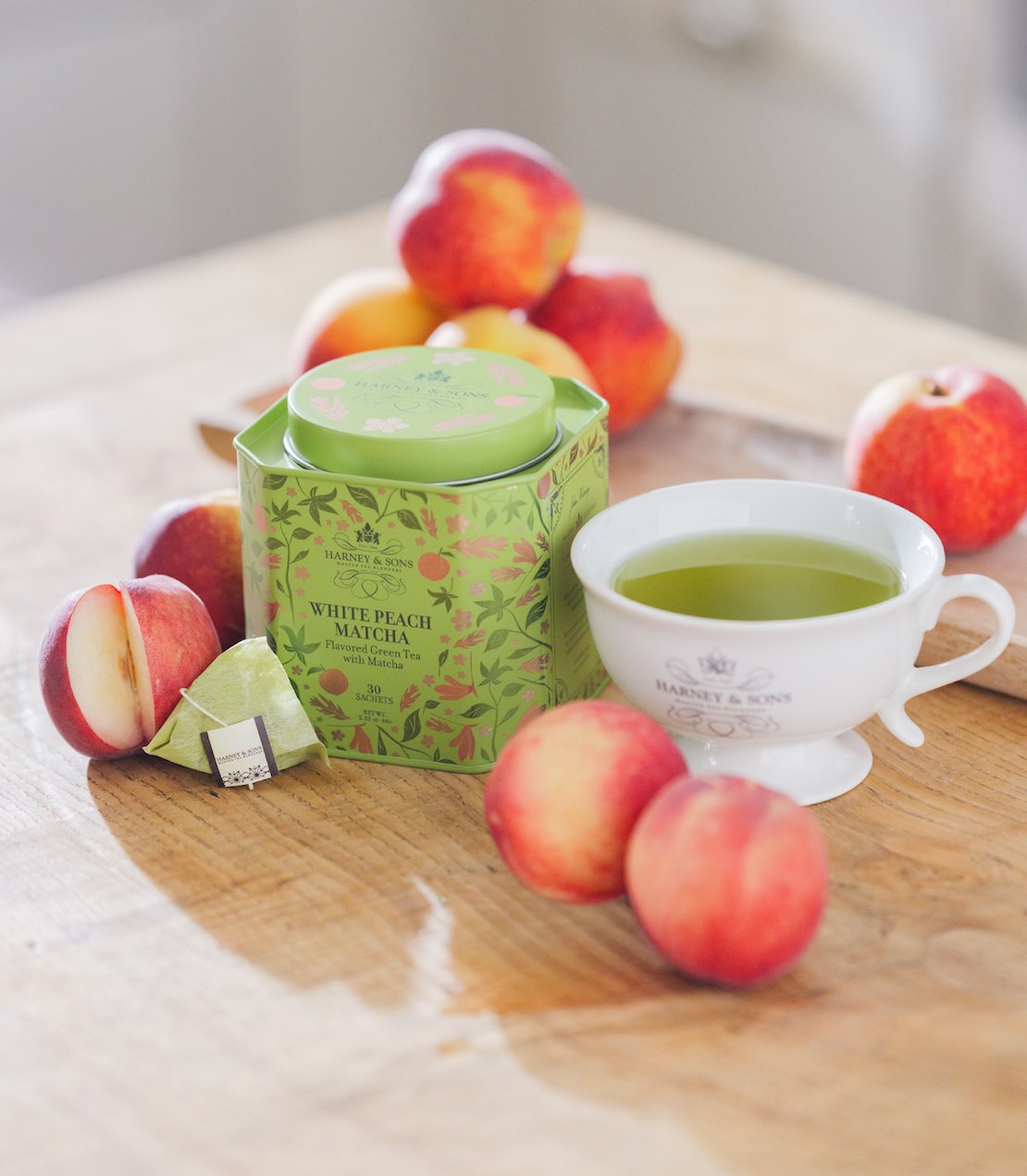 White Peach Matcha tin with a cup of tea and peaches on a wooden surface.