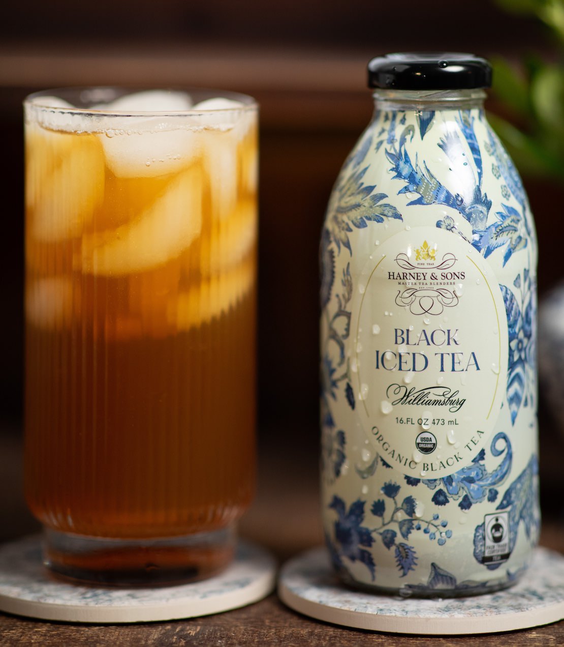 Bottle of Harney & Sons Black Iced Tea next to a glass of iced tea on a wooden surface.