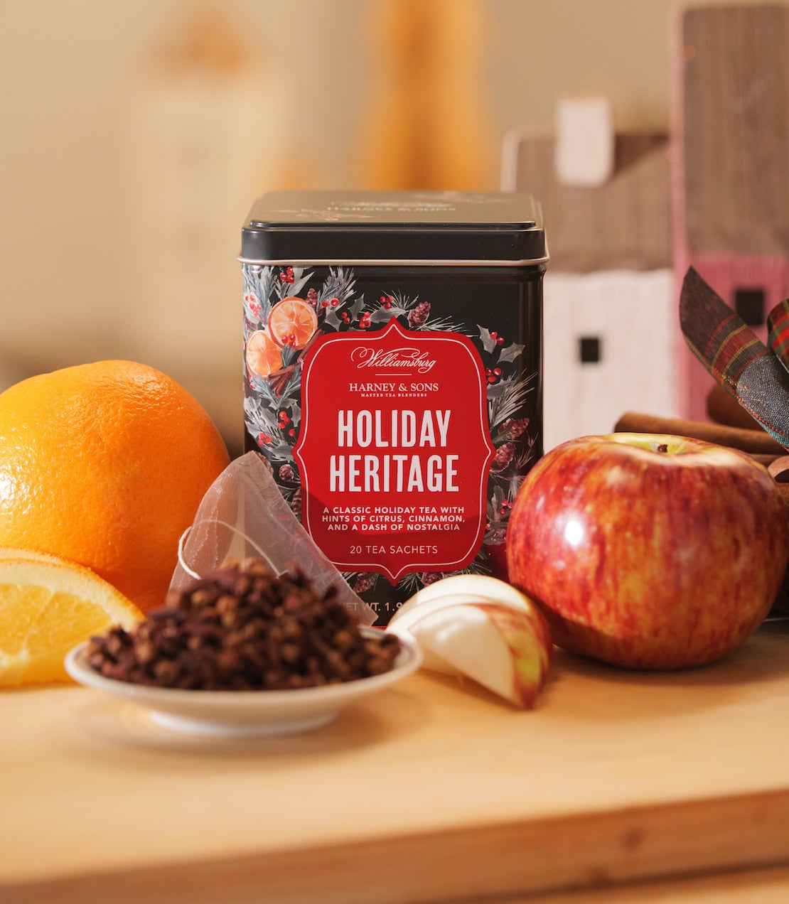 Williamsburg Holiday Heritage Tea tin with 20 sachets, surrounded by apple, orange, and loose tea leaves on a wooden surface.
