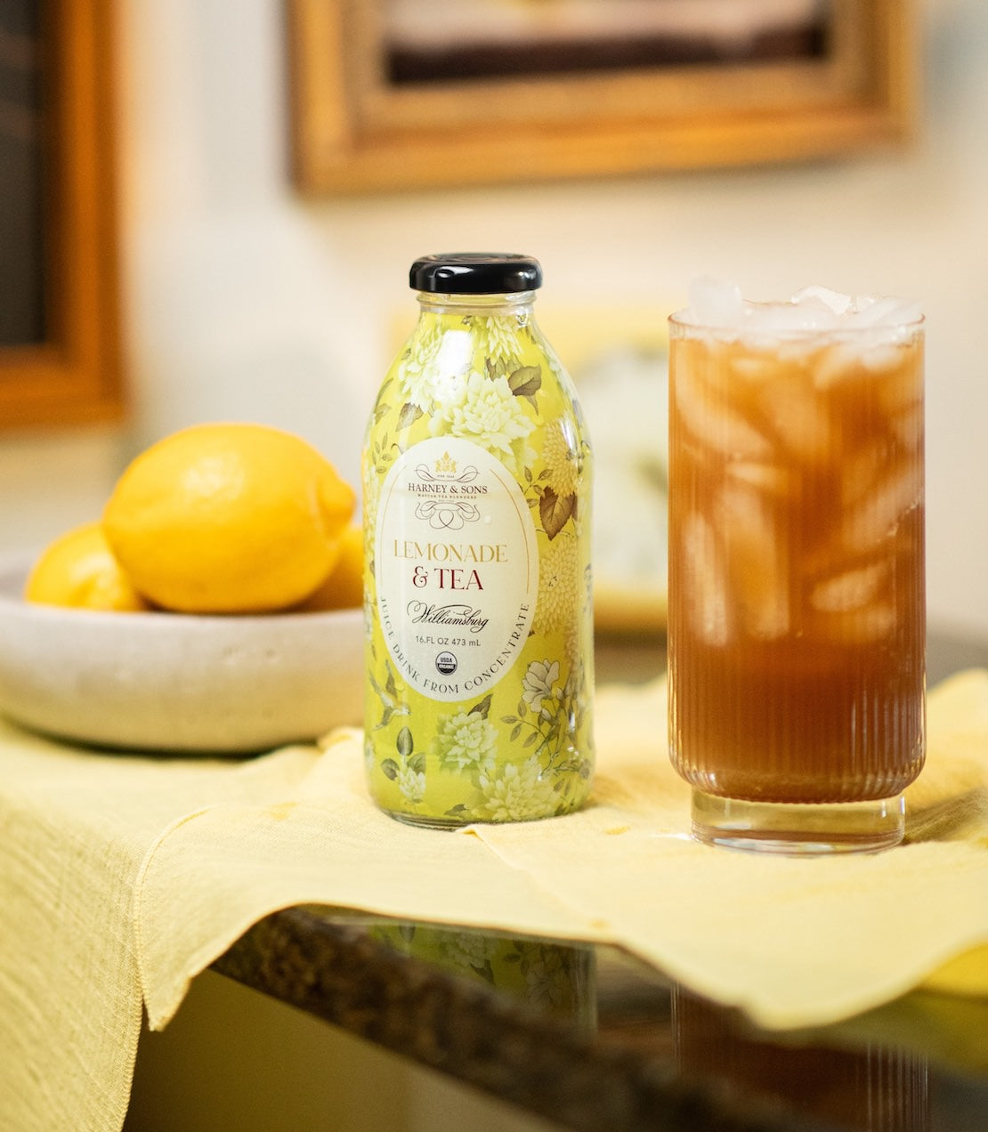 Bottle of lemonade and tea with a glass of iced tea on a table.
