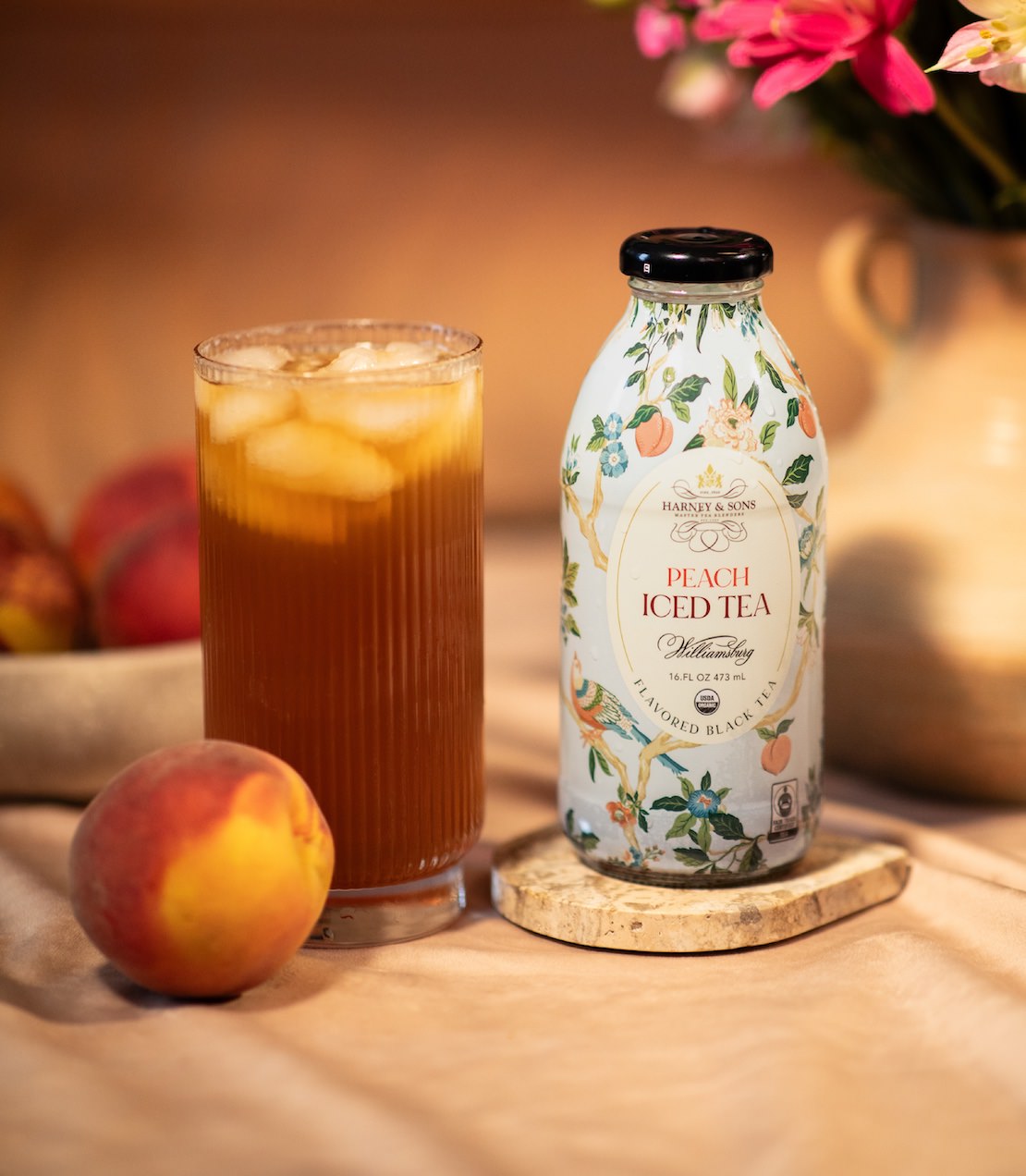 Bottle of Peach Iced Tea with a glass of iced tea and peach on a wooden surface.