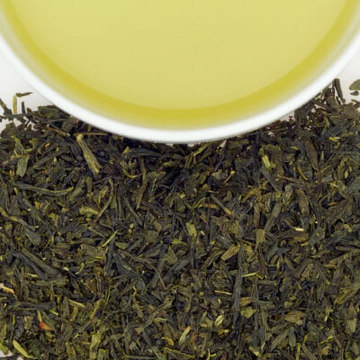 Close-up of loose green herbal tea leaves with a cup of brewed yellow-green tea above.