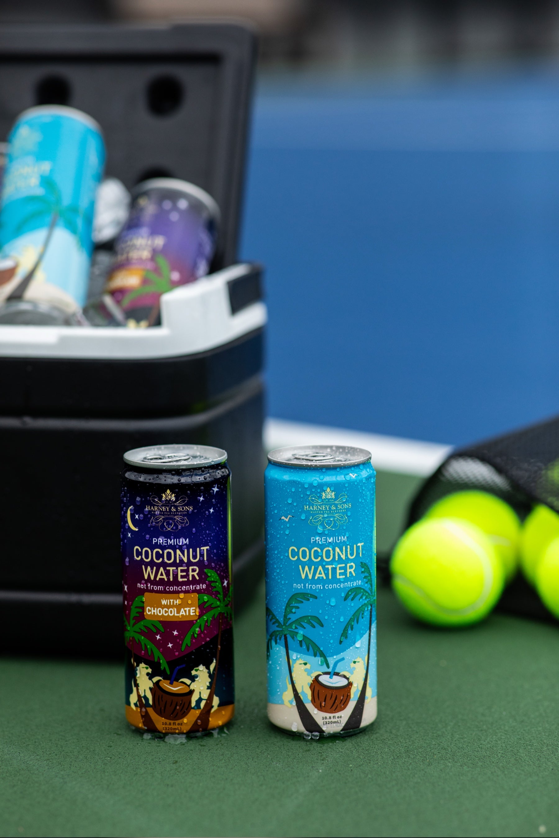 Harney & Sons Premium Coconut Water and Coconut Water with Chocolate cans chilling in a courtside cooler with tennis balls