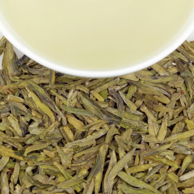 Close-up of loose green tea leaves with a white cup of brewed tea above, highlighting premium herbal tea for connoisseurs.