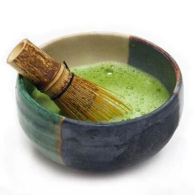 Ceramic bowl with green matcha tea and bamboo whisk, showcasing premium loose tea preparation for connoisseurs.