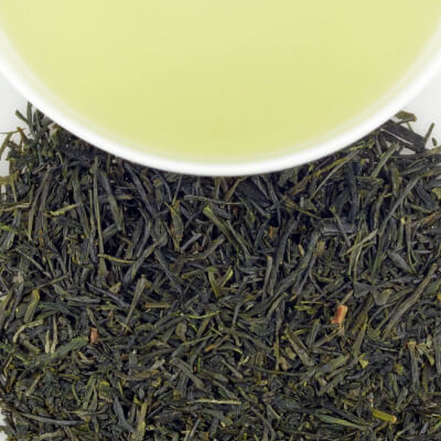 Loose dark green herbal tea leaves with a pale green brewed tea in a white cup above.
