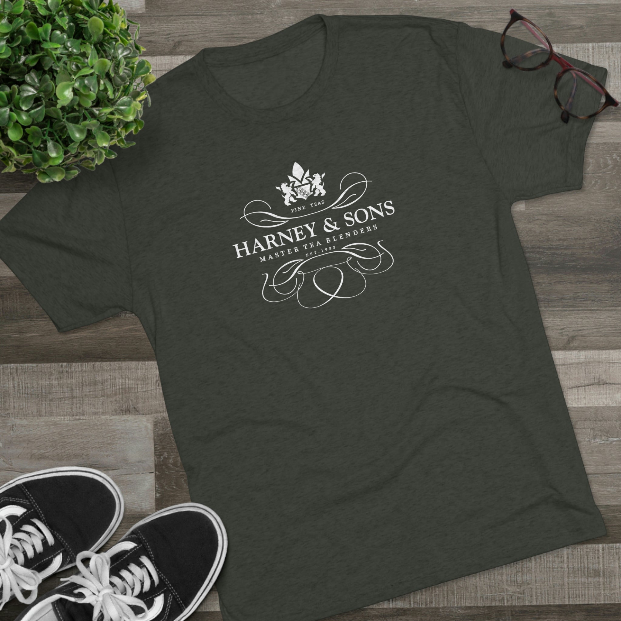 Dark green graphic tee featuring the Harney & Sons logo with elegant design elements, styled with sneakers and glasses.