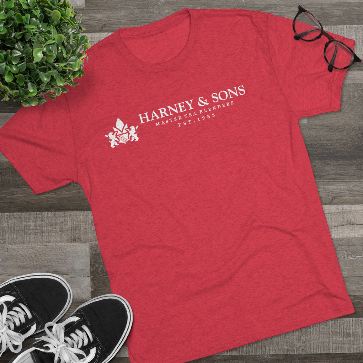 Red graphic tee featuring "Harney & Sons Master Tea Blenders Est. 1983" text, styled with casual shoes and glasses.