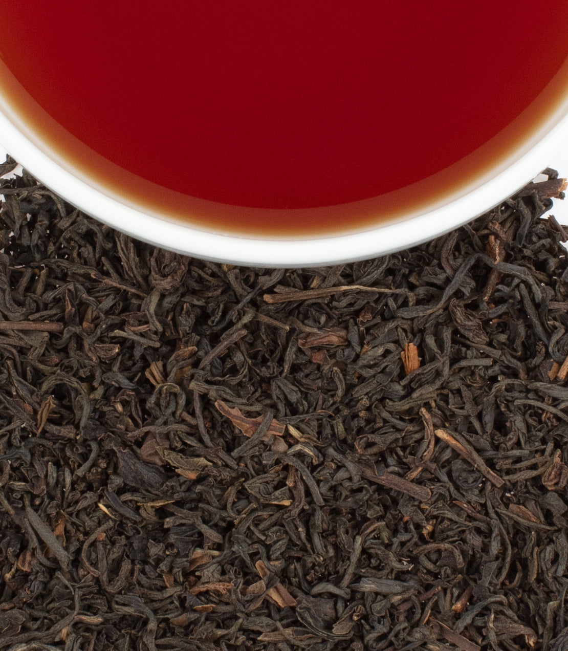 Earl Grey Imperial tea in a cup, surrounded by loose black tea leaves, showcasing rich color and aroma.