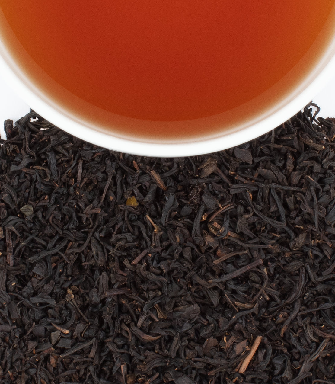 Black currant tea in a white cup above loose black tea leaves, showcasing a rich amber color. Tin of 20 sachets included.