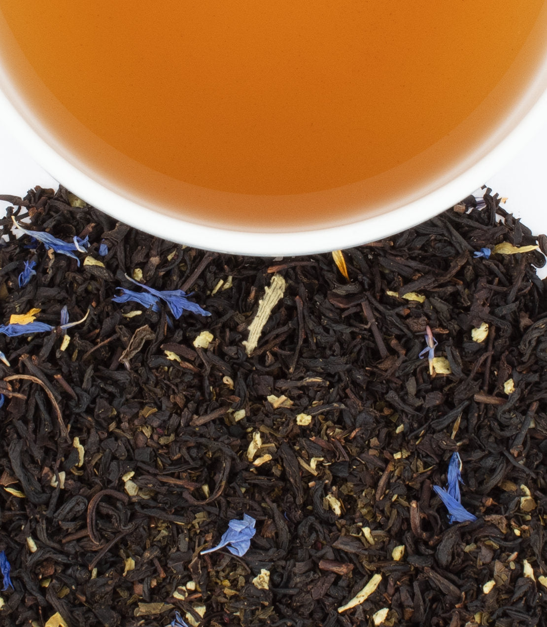 A close-up of loose black tea leaves with blue flower petals, next to a cup of brewed tea.
