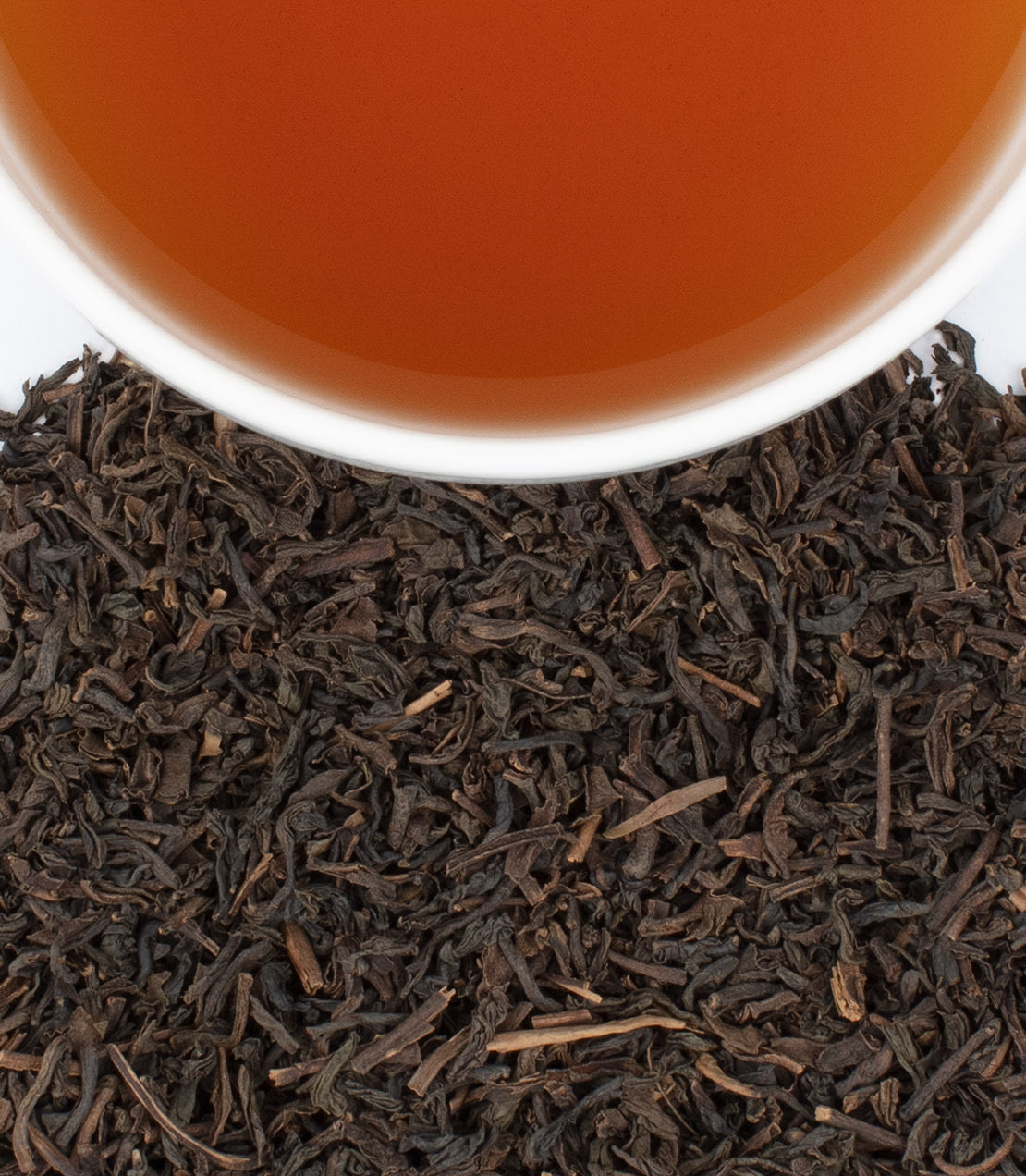 A cup of brewed Decaf Paris tea above loose black tea leaves, showcasing rich color and texture.