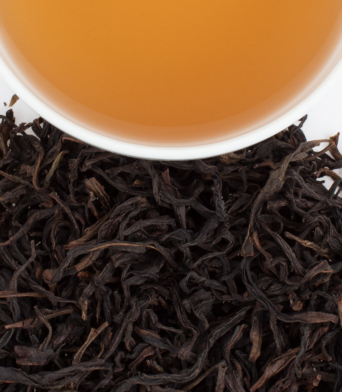 Fenghuang MiLan tea leaves with brewed tea in a white cup, showcasing rich color and texture.