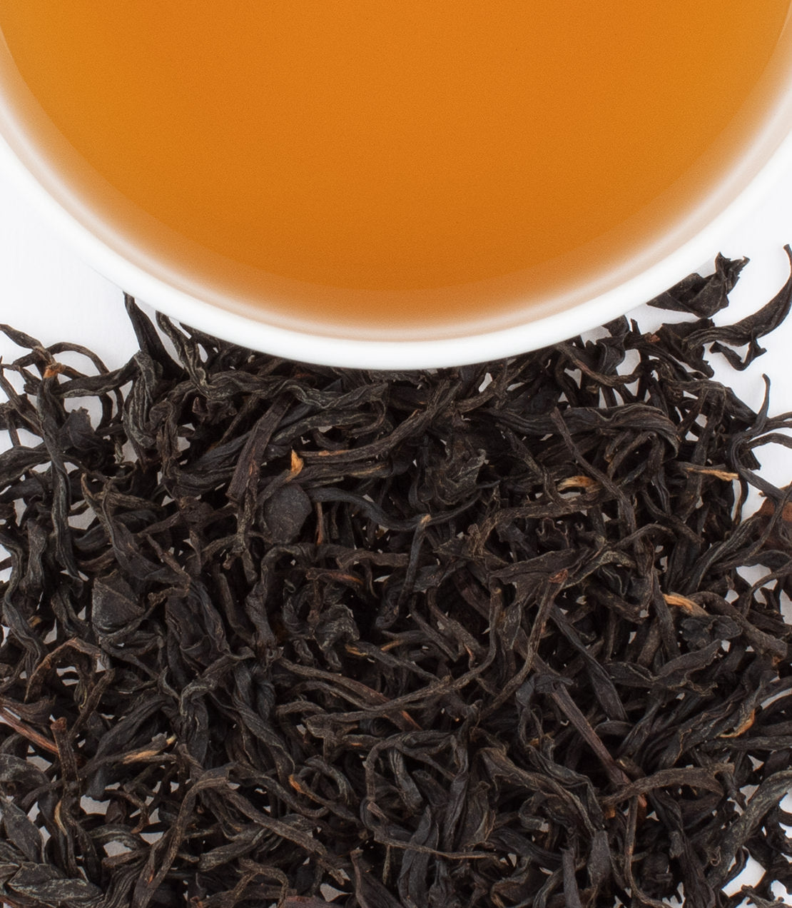 Golden Mudan tea leaves with brewed tea in a white cup, showcasing rich amber color and loose black tea leaves.