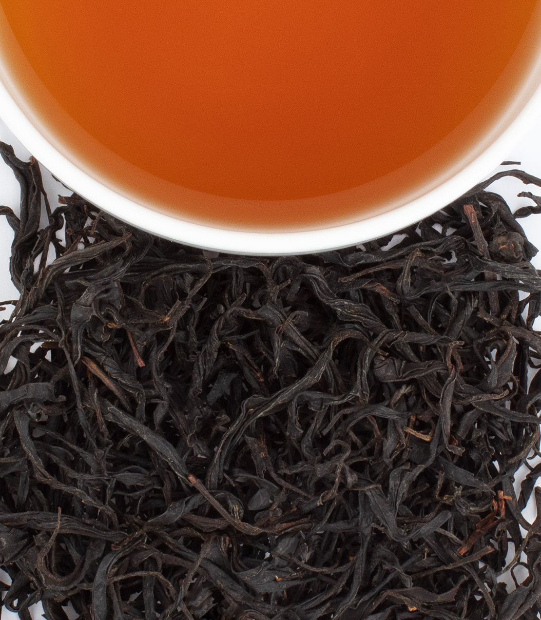 A cup of Louisiana Big Easy Black tea above loose black tea leaves, showcasing rich color and texture.
