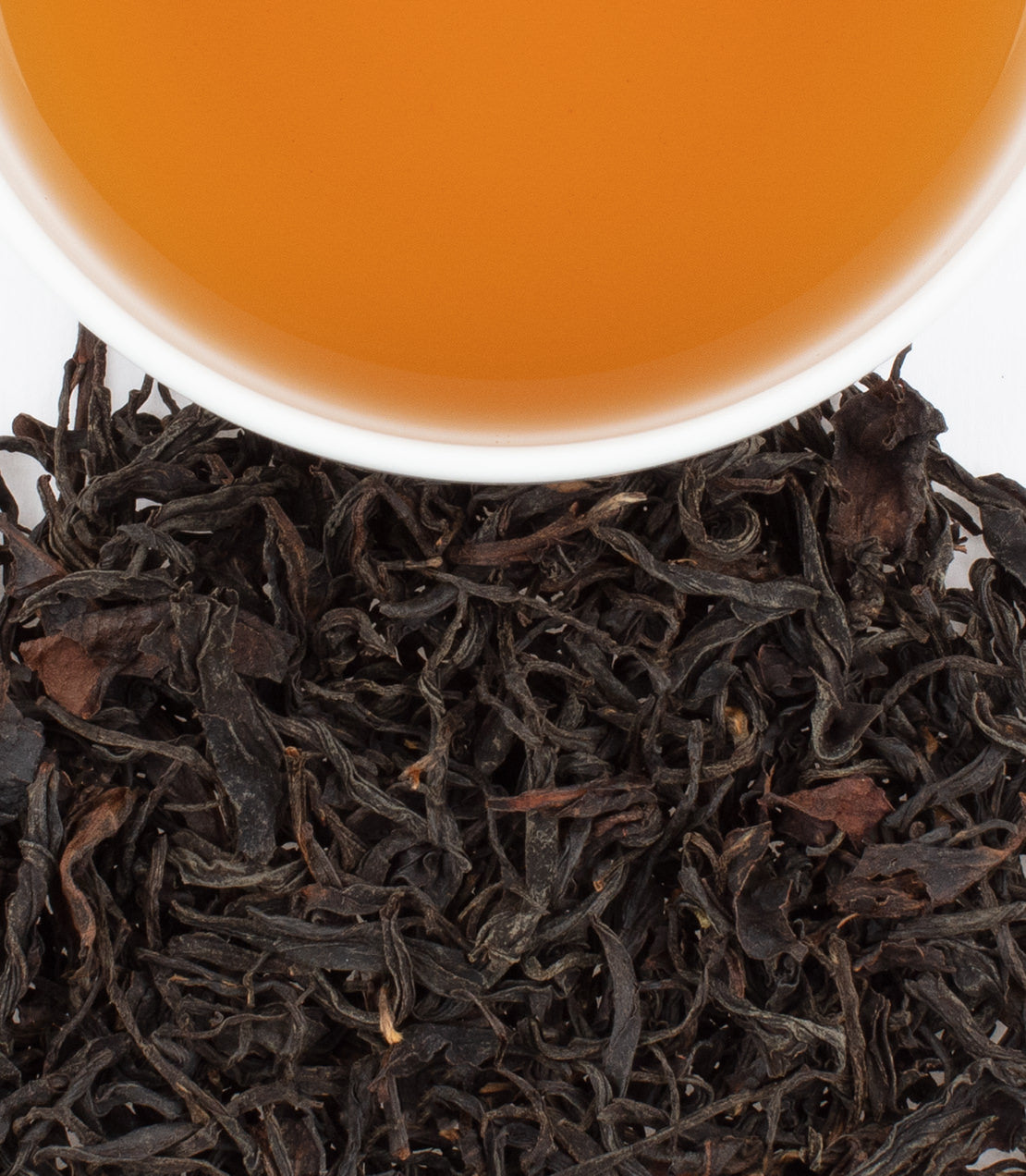 A cup of Wild Wuyi tea above loose black tea leaves, showcasing its rich color and texture.