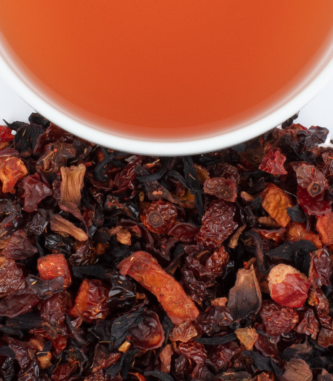 A cup of peach fruit tea above a blend of dried fruits and herbs, showcasing vibrant colors and textures.