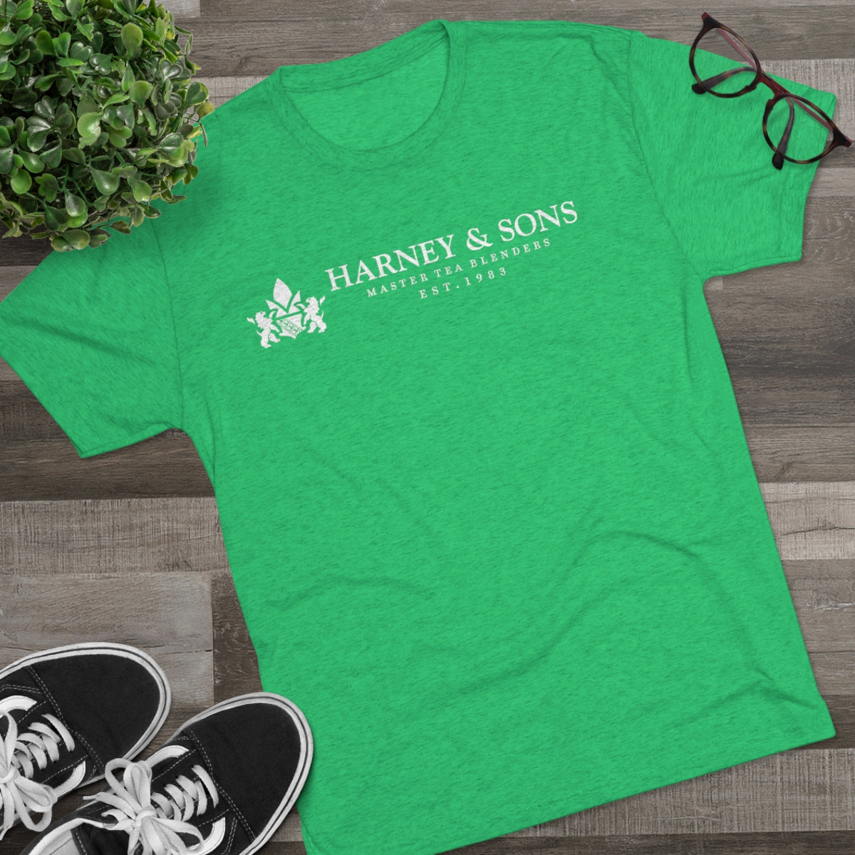 Green graphic tee featuring "Harney & Sons" and "Est. 1983" text, styled with a casual look and accessories.