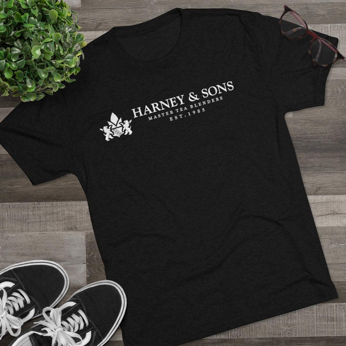 Black graphic tee featuring "Harney & Sons Master Tea Blenders Est. 1983" text, styled with sneakers and glasses.