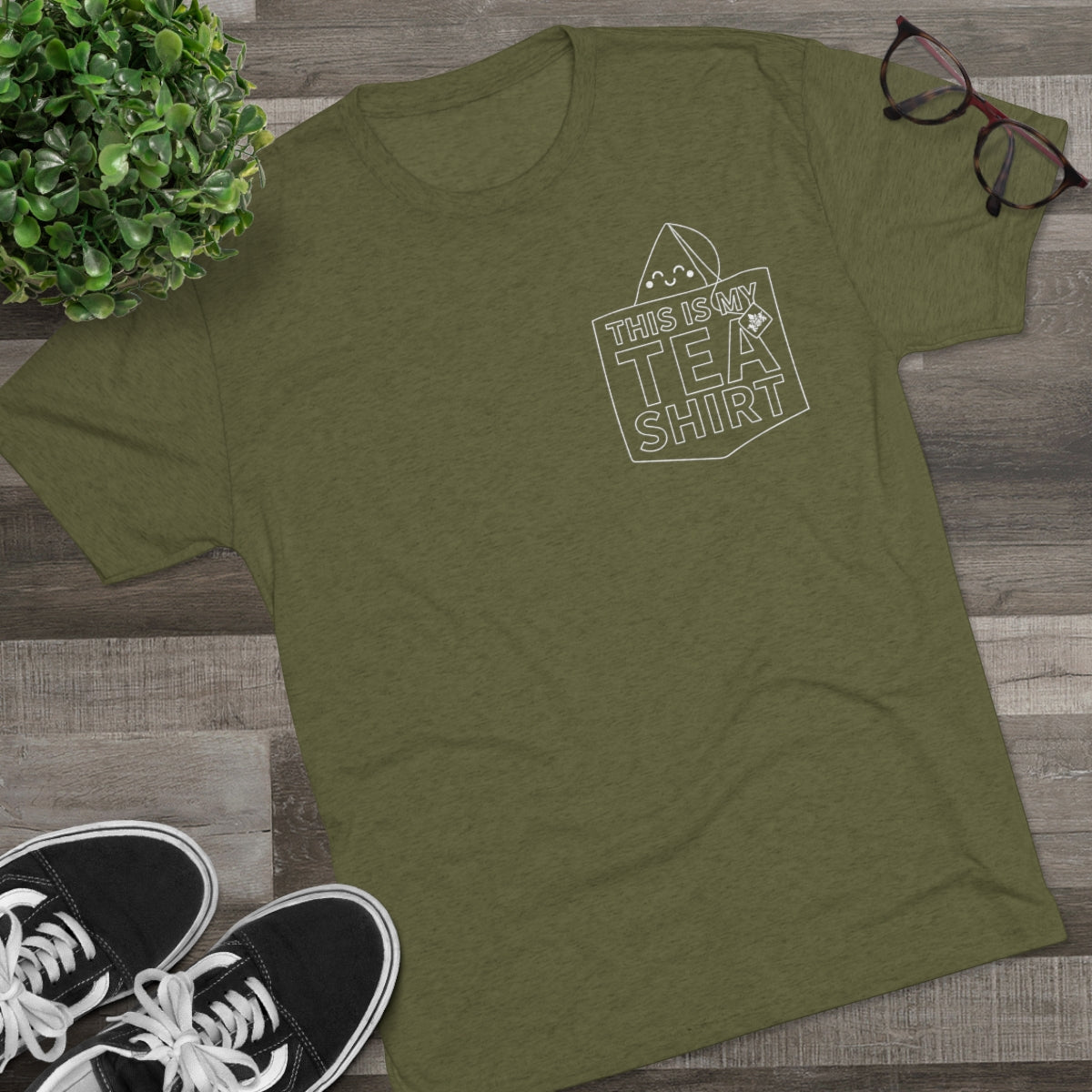 Olive green graphic tee with "This Is My Tea Shirt" text and a tea bag design, paired with sneakers and glasses.
