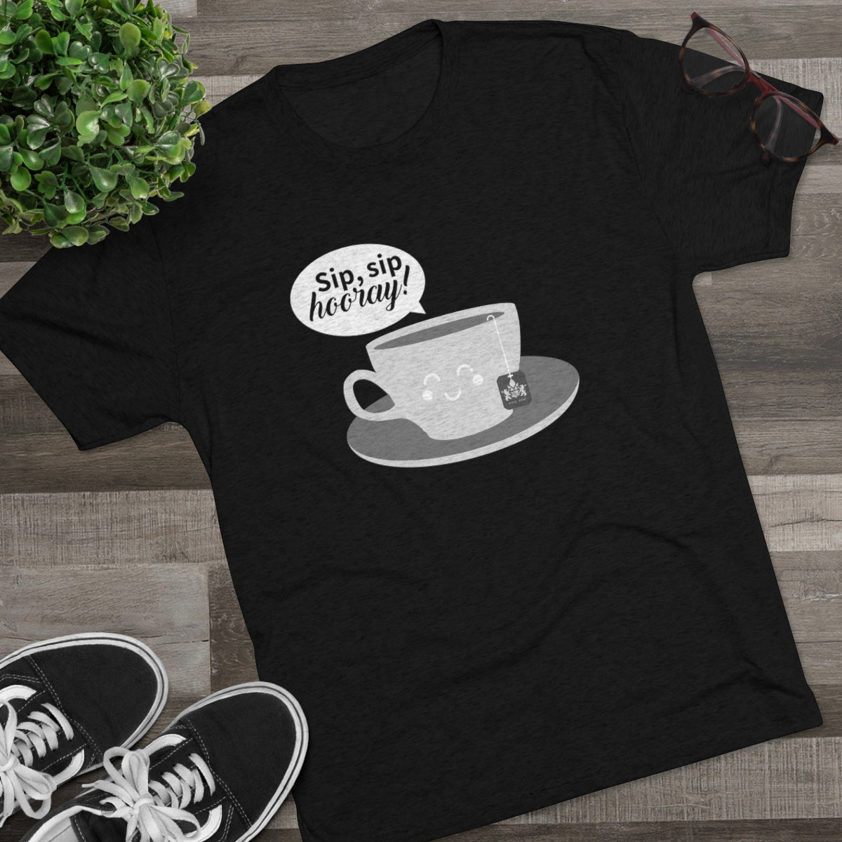 Black graphic tee featuring a cute teacup with the text "Sip, sip, hooray!" and a tea bag, styled with casual shoes and glasses.