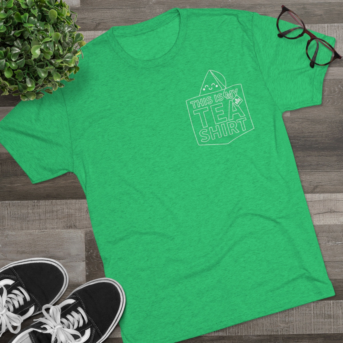 Green graphic tee featuring the text "This Is My Tea Shirt" with a playful design, styled with sneakers and glasses.