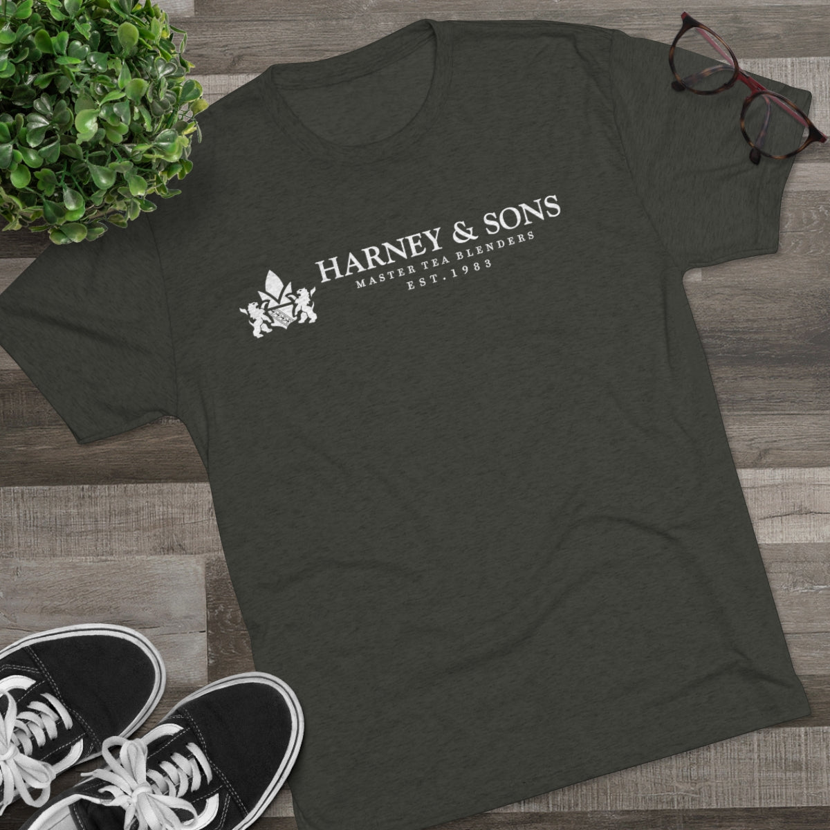 Dark green graphic tee featuring "Harney & Sons Master Tea Blenders Est. 1983" text, styled with casual sneakers and glasses.