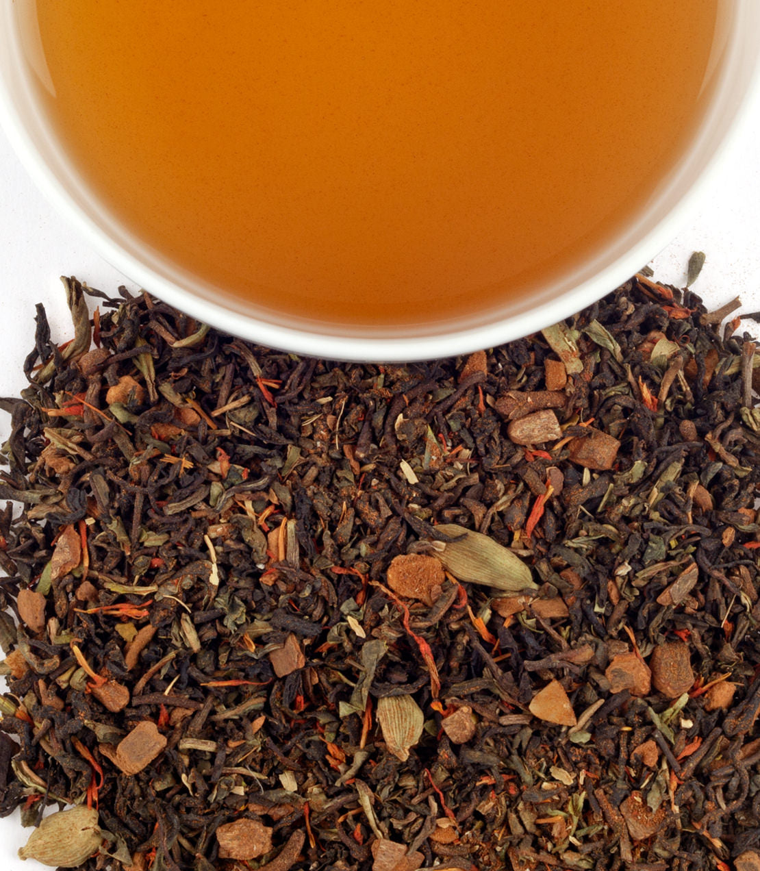 A cup of Kangra Kahwa tea above a pile of loose tea leaves and spices, showcasing its rich color and texture.