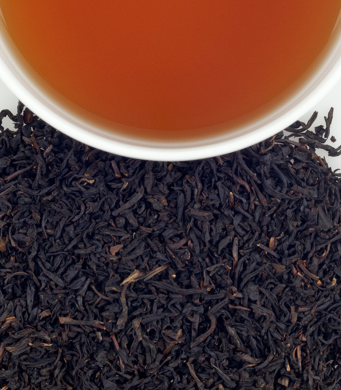 A close-up of dried black tea leaves with a cup of brewed tea above, showcasing rich colors and textures.