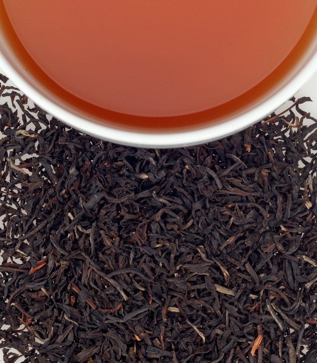 Rwandan Rukeri black tea leaves with brewed tea in a white cup, showcasing rich color and texture.