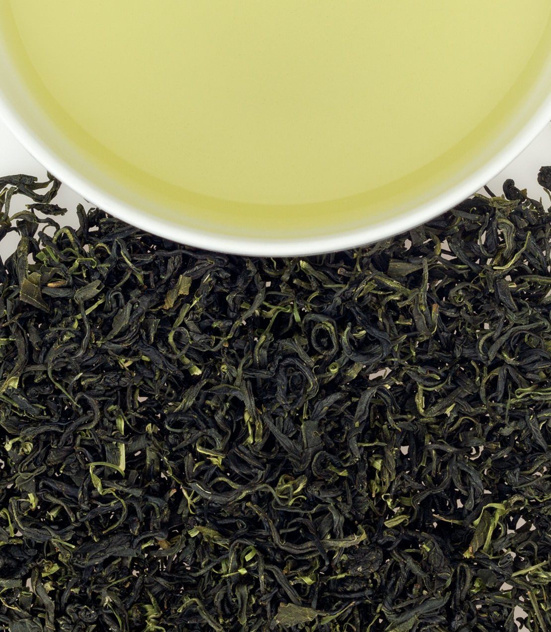 Fresh Jeju Sejak green tea leaves with brewed tea in a white cup, showcasing vibrant green hues.