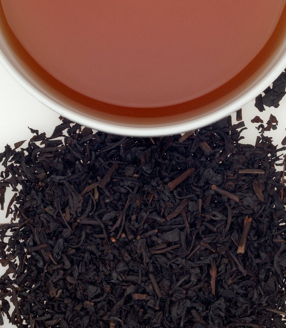 A cup of brewed smoke tea above a pile of loose black tea leaves, showcasing rich color and texture.