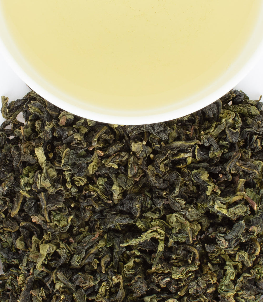 Autumnal Ti Quan Yin tea leaves with a cup of light yellow brew, showcasing the rich texture and color.