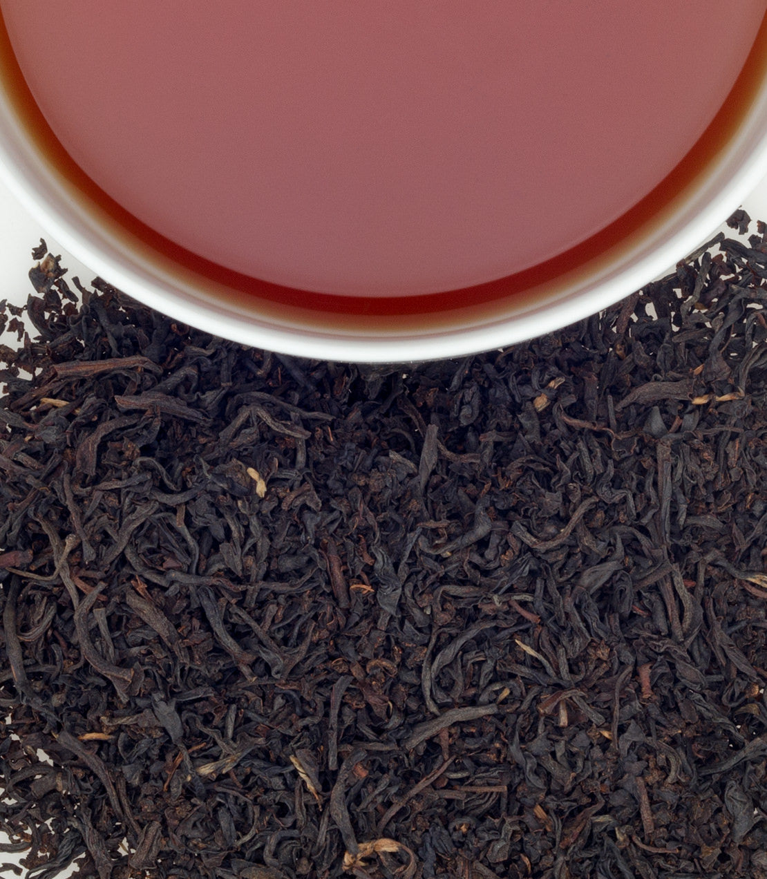 "English Breakfast tea in a cup above loose black tea leaves, showcasing a rich color and aroma.