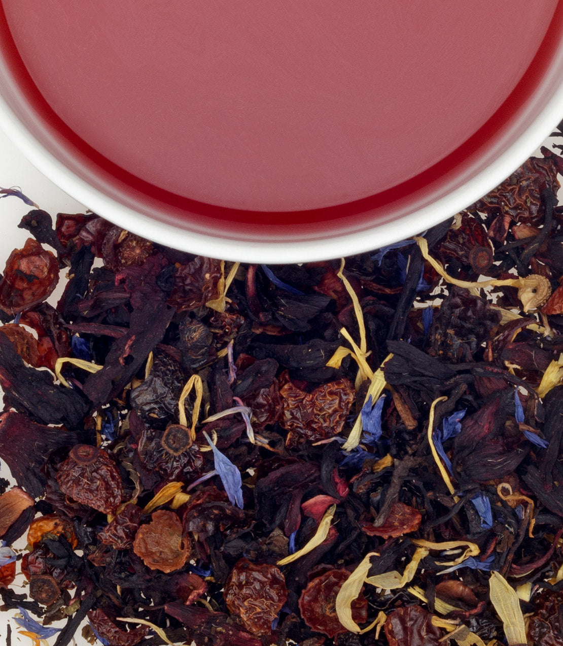 A cup of vibrant red birthday tea surrounded by colorful dried tea leaves and flowers.