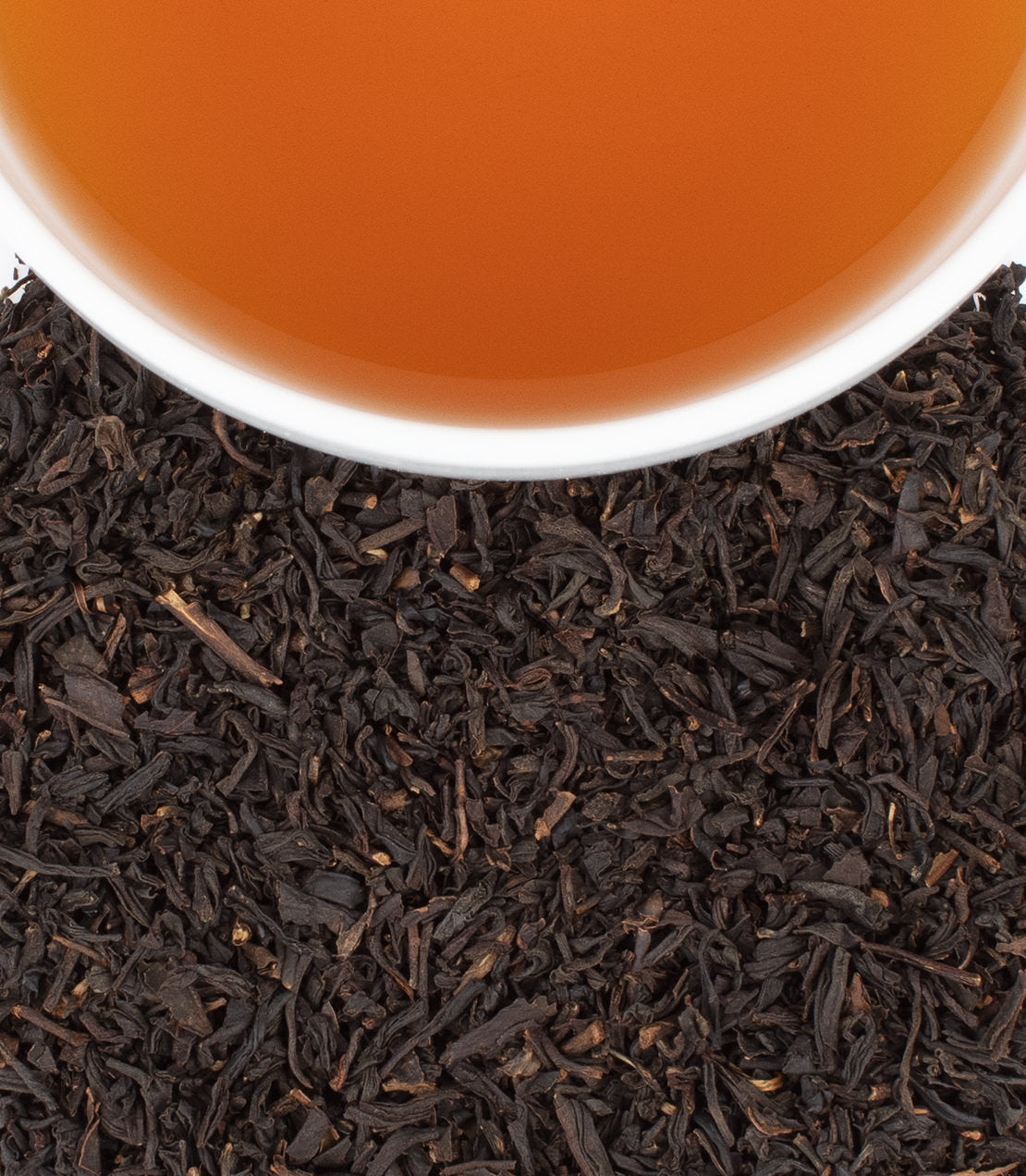Rich amber bourbon in a glass, surrounded by dark, loose tea leaves, showcasing a blend of flavors.