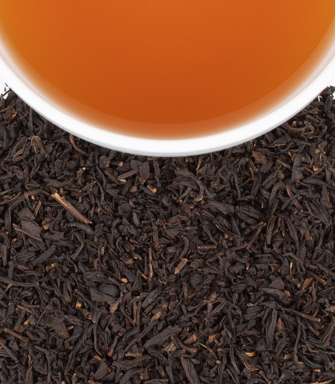 Black Cask Bourbon tea in a cup, surrounded by loose black tea leaves, packaged in a bag of 50 sachets.