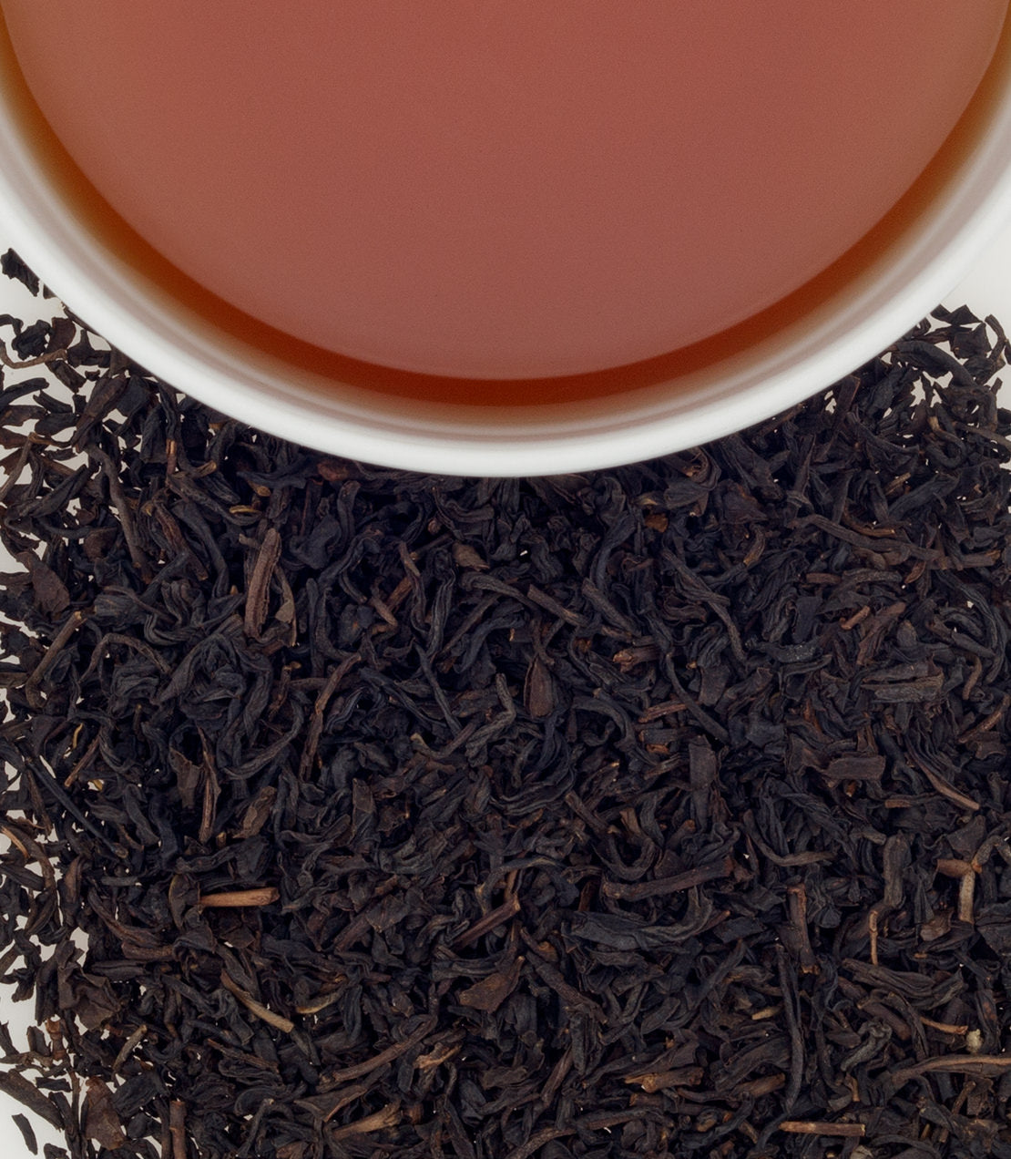 A cup of brewed black jasmine tea above loose black tea leaves, showcasing rich color and texture.